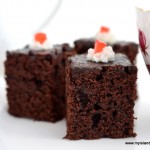 Three chocolate brownies with a dob of icing and red cherries set against a white background