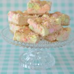 Glass pedestal dish filled with confetti-colored mini marshmallow squares set against a turquoise and white checked background