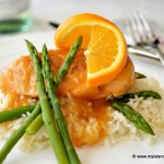Maple-Orange Sauced Chicken Breast on top of a bed of white rice served with green asparagus and an orange wheel