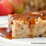 A piece of Bread Pudding drizzled with Maple Sauce sits on plate in front of a background of apples