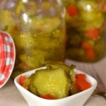 Small white dish containing bread and butter pickles sits in front of pickle jars