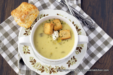 Potato Leek Soup garnished with croutons and a sprinkle of parsley in white bowl alongside a homemade biscuit