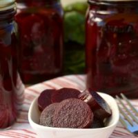 Jars of pickled beets in the background with a small serving dish filled with beets in the foreground