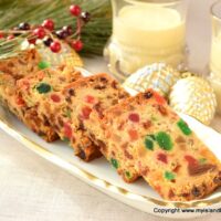 Tray with slices of light fruitcake and glasses of eggnog in the background