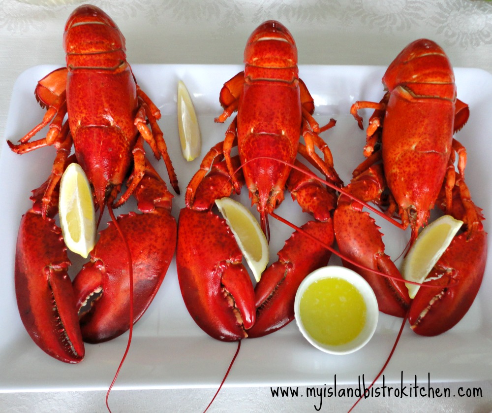 Three steamed lobster on white tray with wedges of lemon and a small bowl of melted butter for dipping the lobster meat