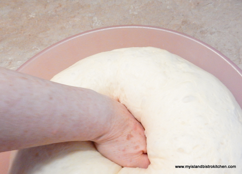 Fist in center of risen dinner roll dough punching it down inside a pink bowl