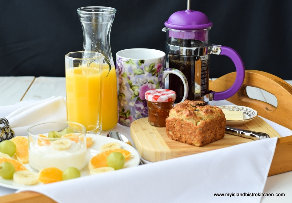 Gluten-free Banana Date Muffin on Breakfast Tray with a Carafe and Glass of Orange Juice, Plate of Fresh Orange, Grapes, and Yogurt, and French Press Coffee