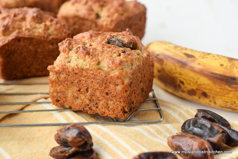 Large, perfectly domed Gluten-free Banana Date Muffins on a cooling rack surrounded by dates and a ripe banana