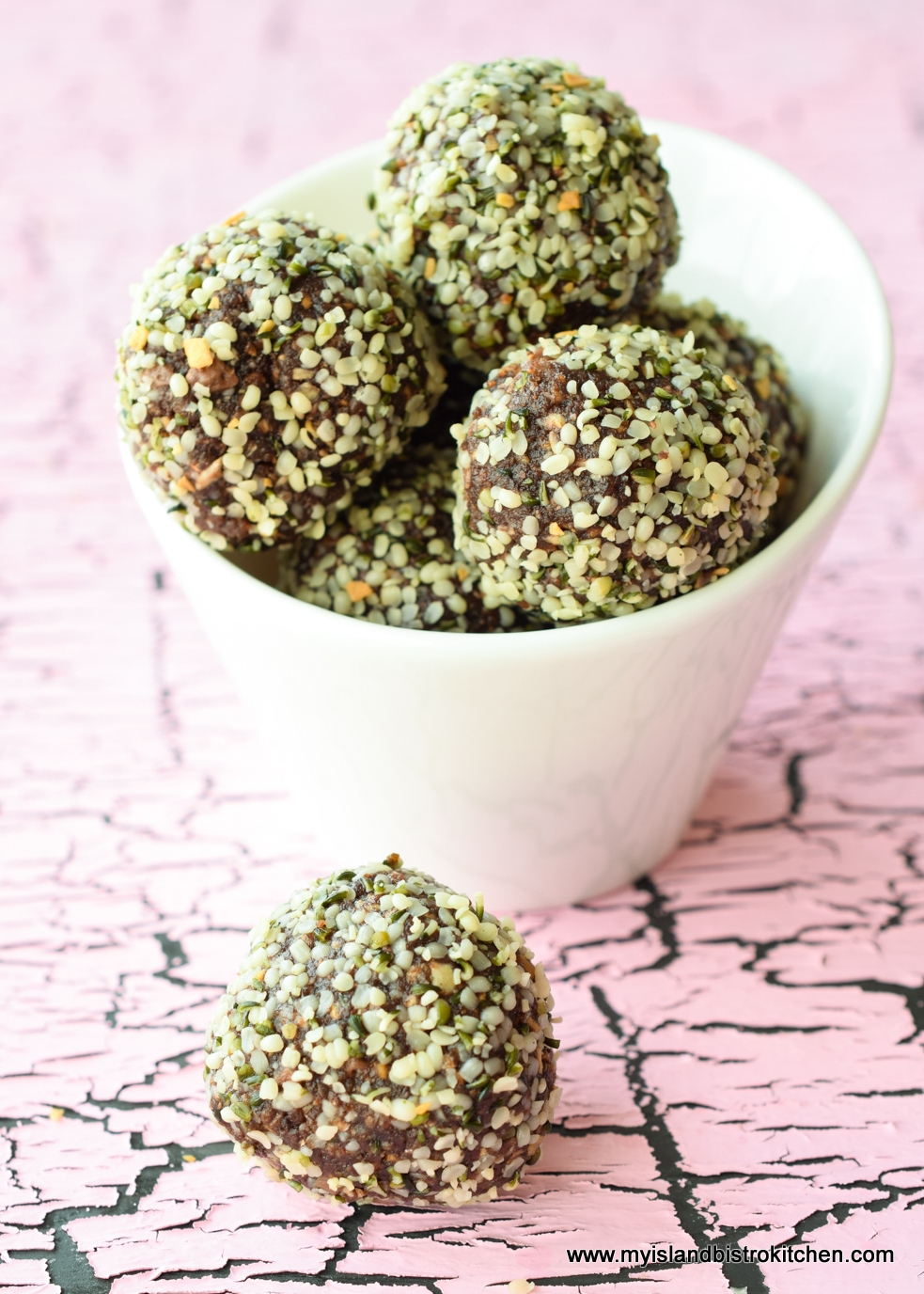 Small white bowl filled with No-bake Chocolate Almond Bliss Balls Rolled in Hemp Hearts set against a pink and gray backdrop