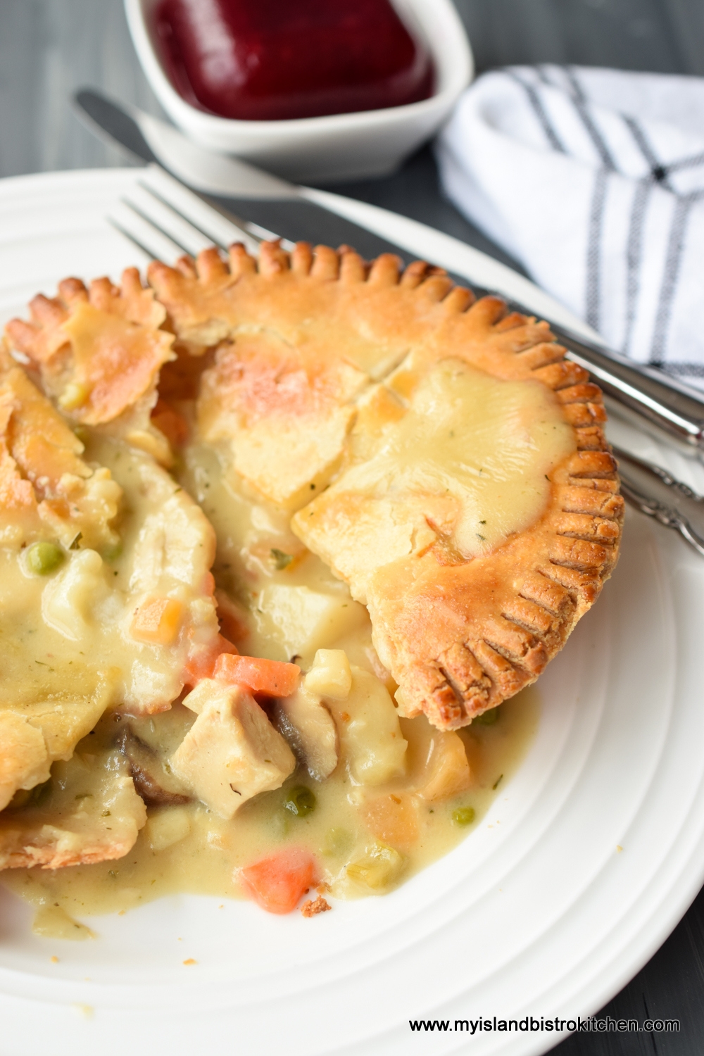 Individual chicken pot pie on white dinner plate with knife and fork in background