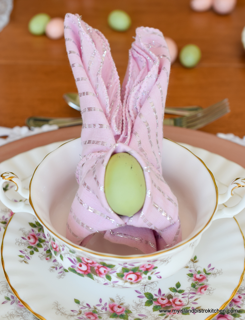 Pink napkin is folded into the shape of bunny ears and placed inside a soup bowl at an Easter-themed tablescape