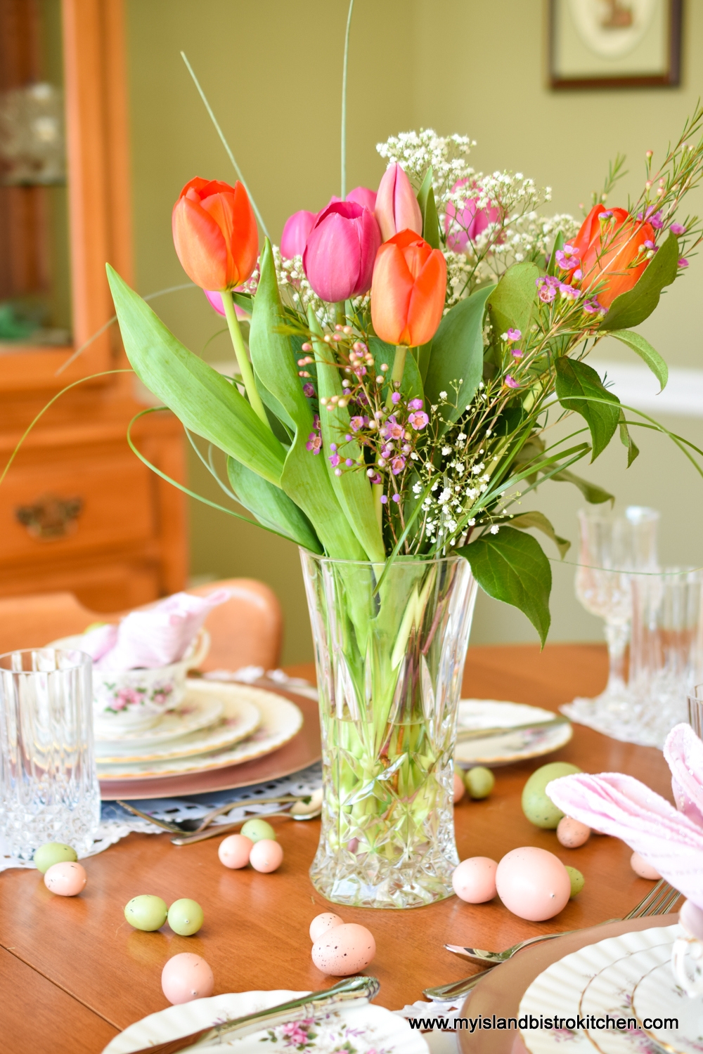 Large glass vase filled with bright pink and orange tulips in the center of a table