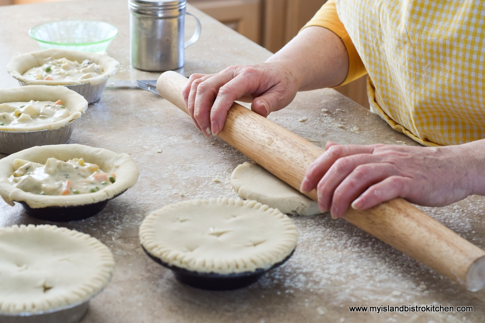 Hands rolling pie pastry with small chicken pot pies in the foreground