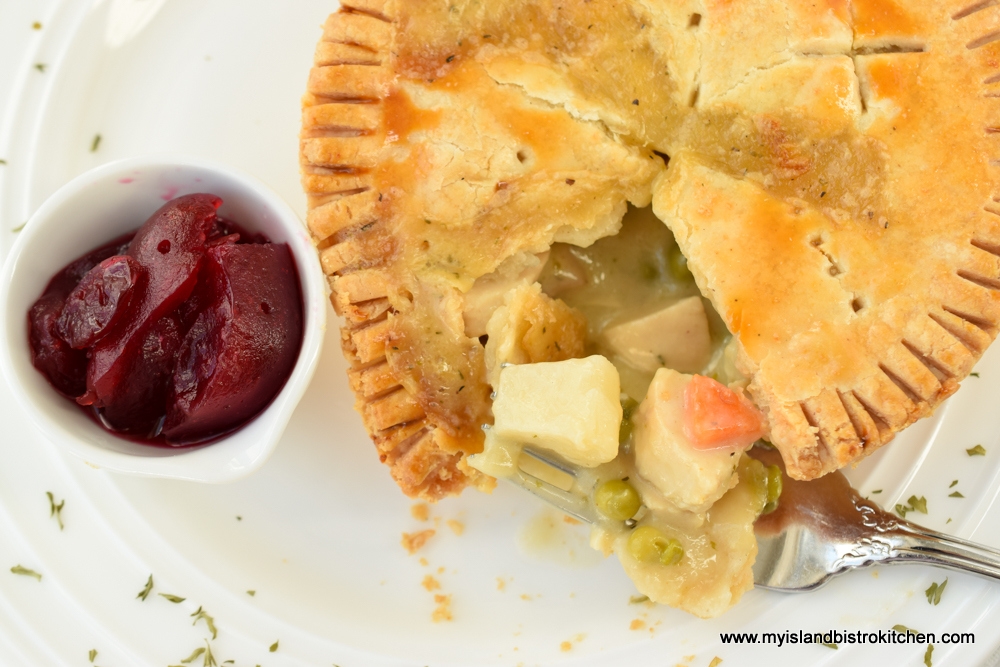 Individual chicken pot pie on white dinner plate with a small dish of cranberry sauce