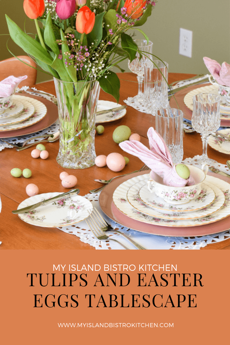 Easter-themed tablesetting with Royal Albert "Lavender Rose" dinnerware on pink charger plates. Napkin fold is the bunny ear fold with pink napkins. A large crystal vase of pink and orange tulips is in center of table.