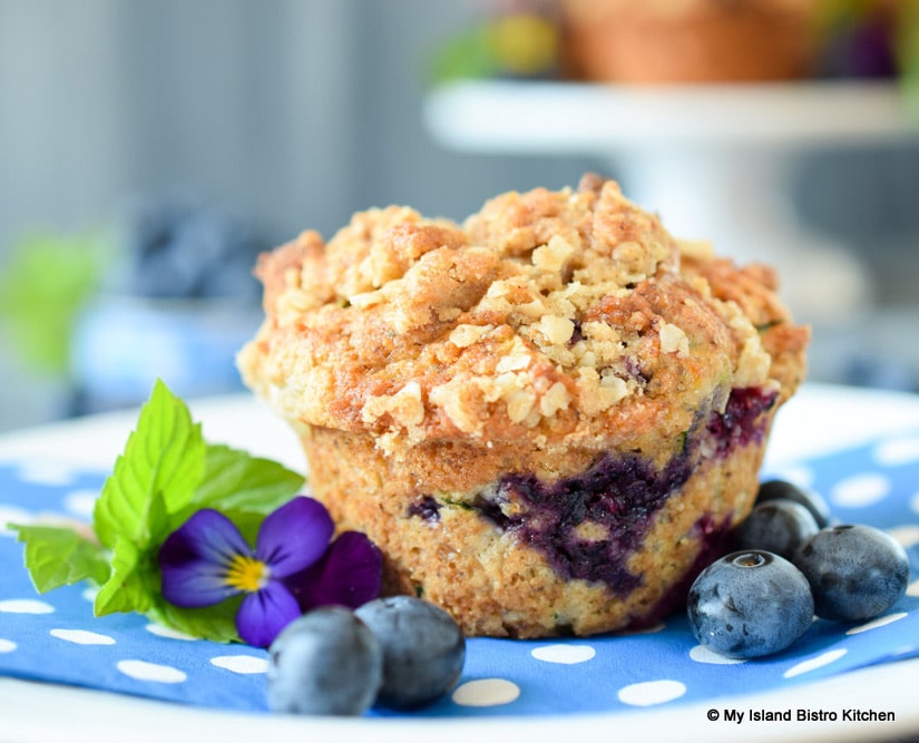 Close-up of a streusel-topped gluten-free Blueberry Zucchini Muffin on blue and white dotted napkin