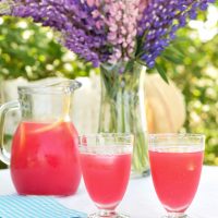Jug and glasses of rosy lemonade beside bouquet of lupins