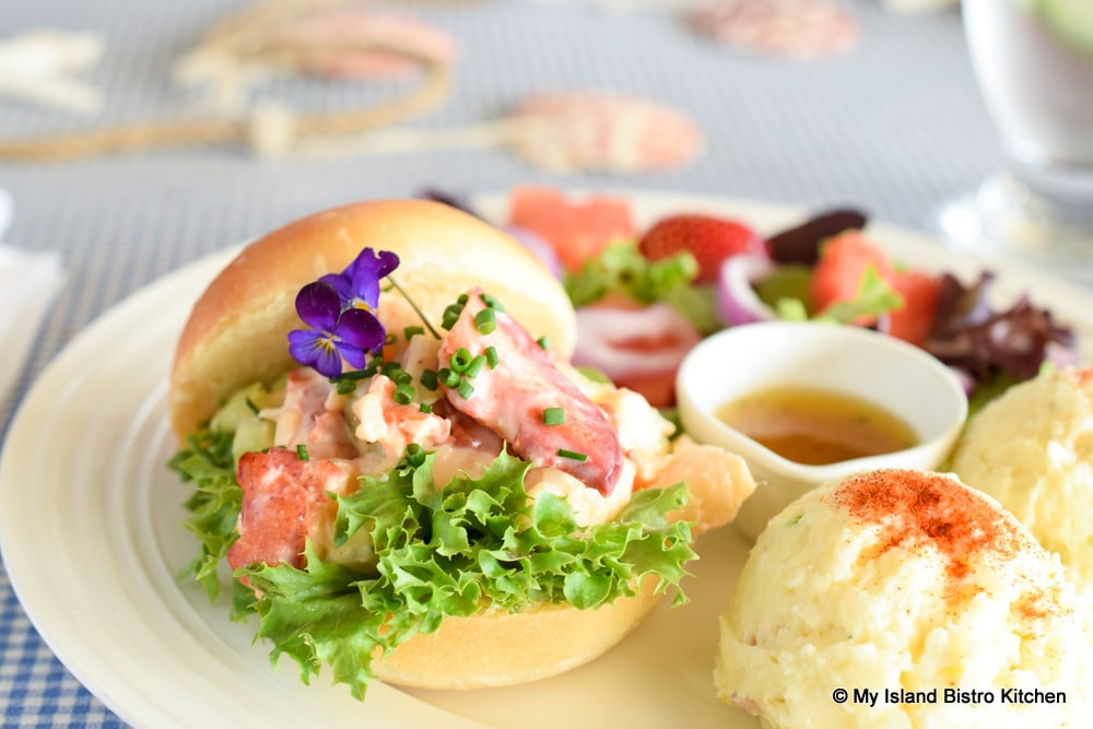 Lobster filling on a bed of green leafy lettuce sandwiched between a homemade hamburger roll