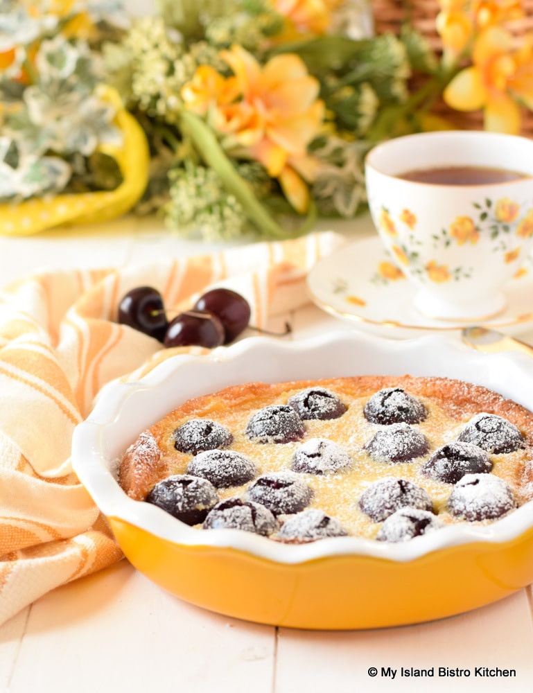 Cherry Clafoutis in yellow pie plate with a cup of tea for teatime
