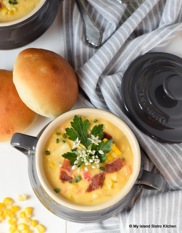 Small casserole filled with golden corn chowder accompanied by homemade rolls