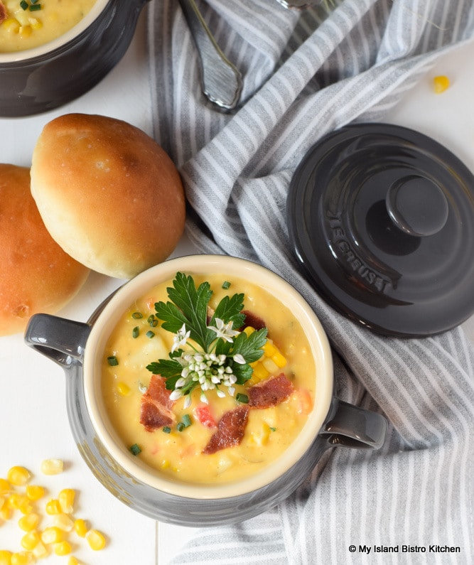 Individual casserole filled with creamy corn chowder accompanied by homemade rolls