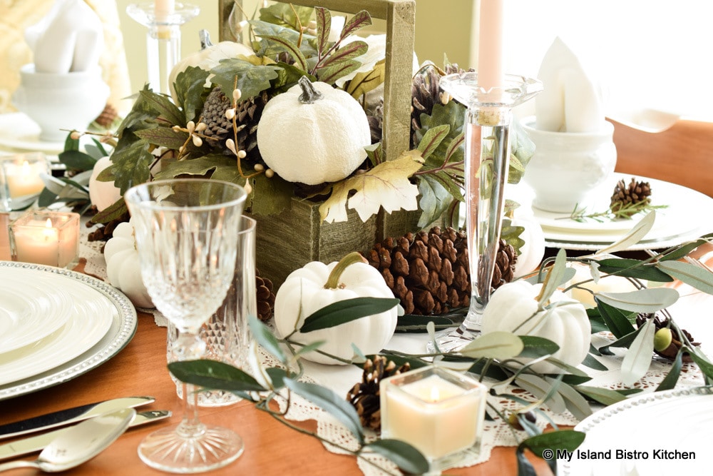 White pumpkins, shades of green, and brown pine cones are the theme for this fall tablesetting
