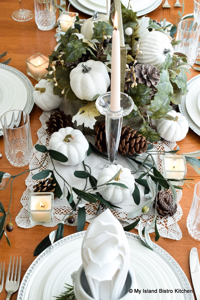 Tiny white pumpkins, faux greenery, and pinecones form the centerpiece for this tablesetting prepared for a fall dinner