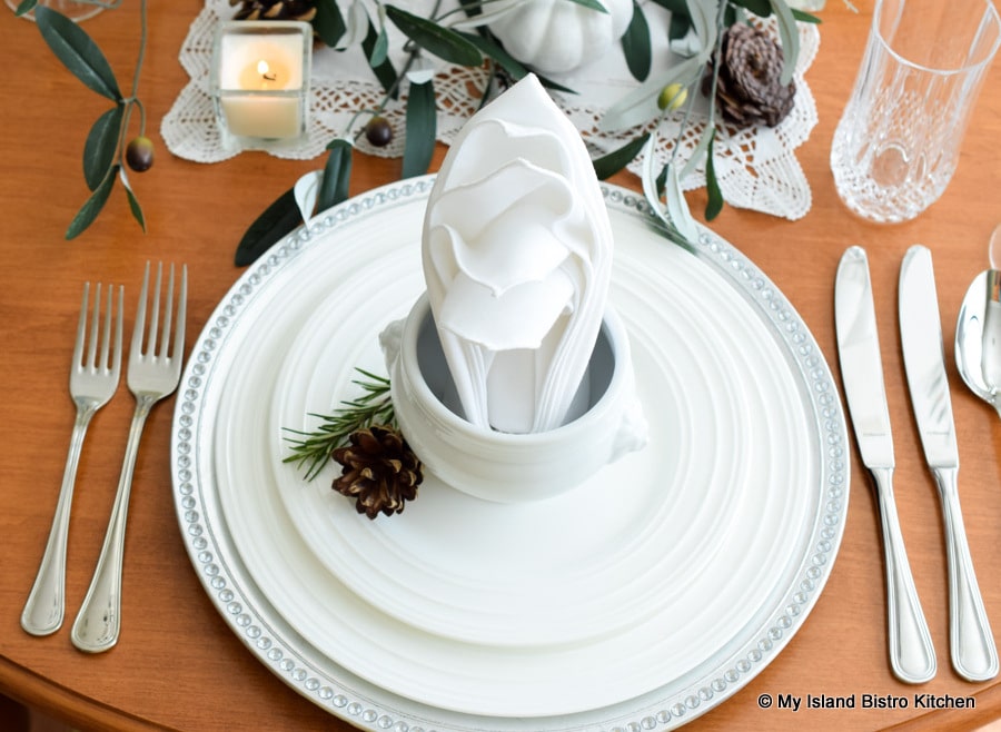 Top-down view of placesetting formed with white dinnerware and silver charger