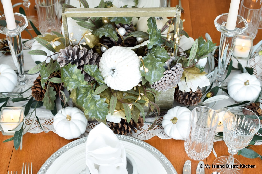 A rustic box of faux autumn greenery, pinecones, and white pumpkins