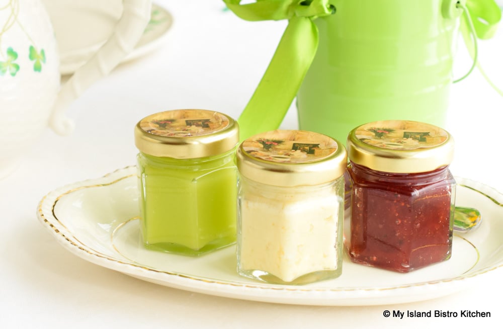 Three small serving jars filled with Lime Curd, Clotted Cream, and Strawberry Jam