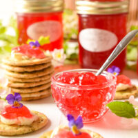 Pretty red jelly in glass bowl with jars of the jelly in the background