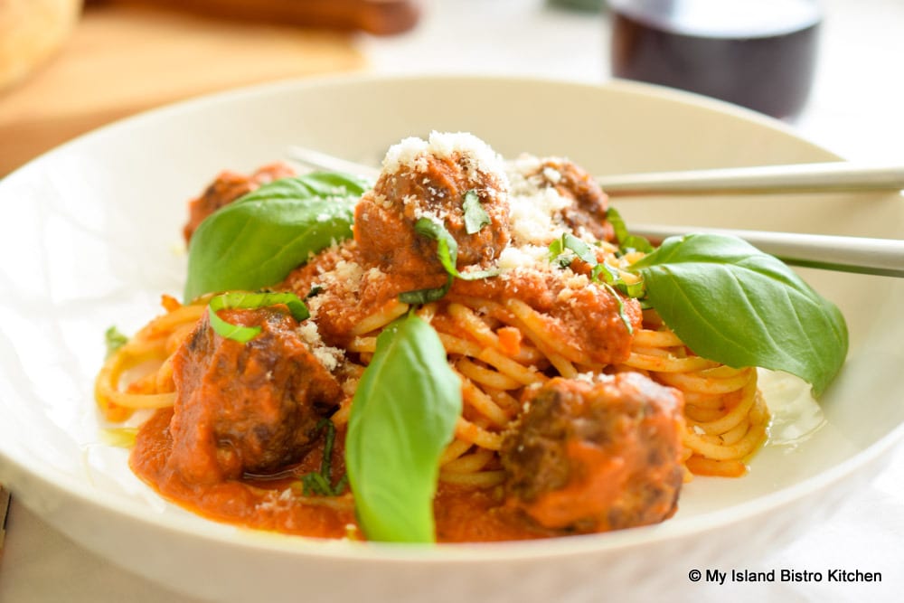Bowl of spaghetti and meatballs in tomato sauce and garnished with fresh basil leaves