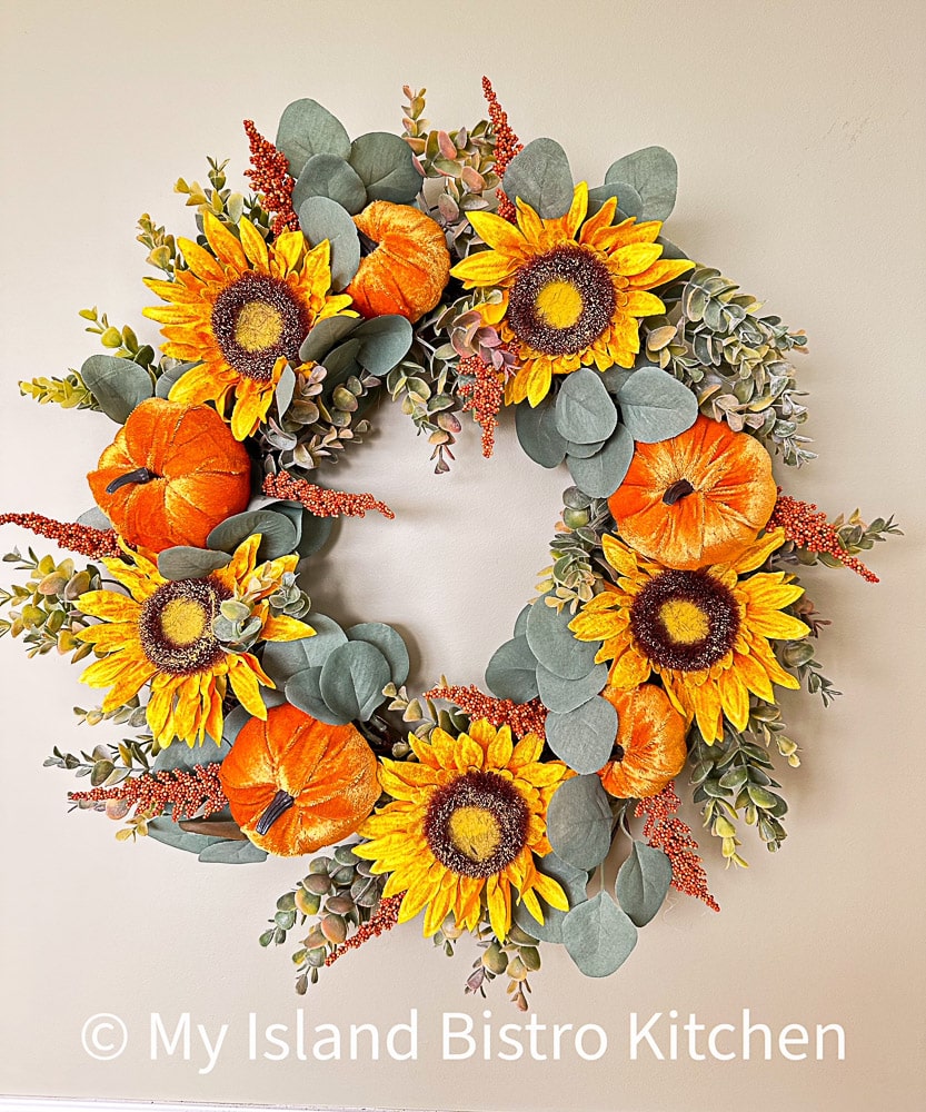 Wreath of yellow sunflowers and orange velvet pumpkins against a background of green Eucalyptus