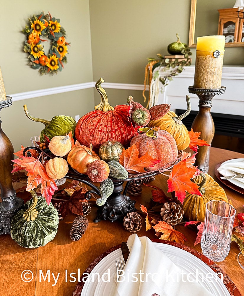 Autumn centerpiece for table consisting of a variety of pumpkins, colored leaves and pinecones all flanked by two tall pillar candles