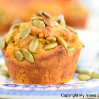Pumpkin Muffin sprinkled with roasted pumpkin seeds sits atop a blue floral plate