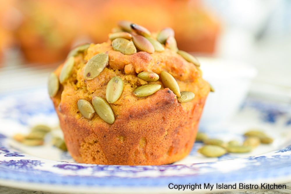 Pumpkin Muffin sprinkled with roasted pumpkin seeds sits atop a blue floral plate