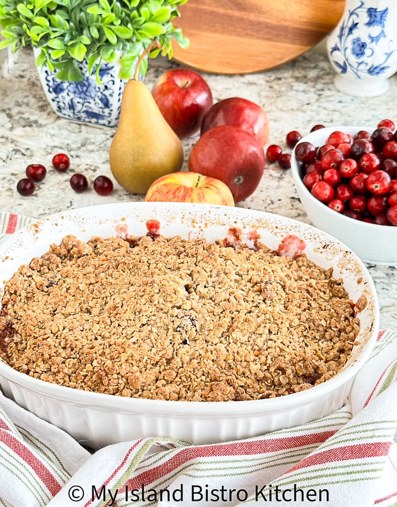 Baked Fruit Crisp sits on counter surrounded by a bowl of cranberries, apples, and Bosc Pear