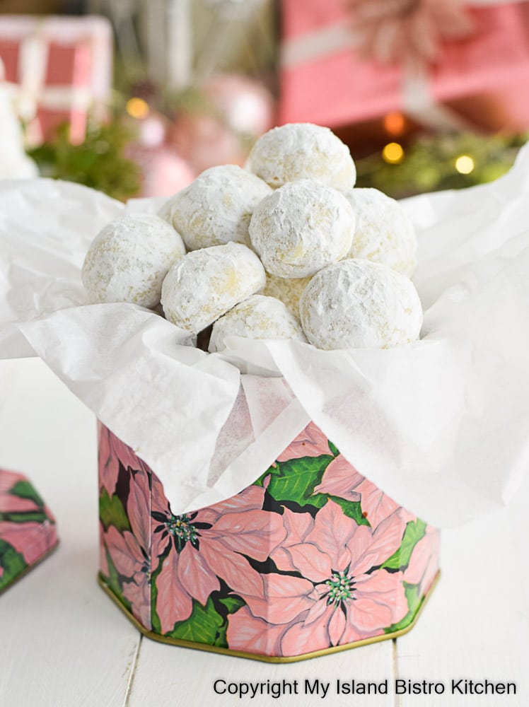 A pyramid of Swedish Tea Cakes surround by holly and cedar on a piece of wood. Wrapped parcels appear in the background