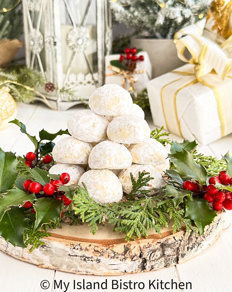 A pyramid of Russian Tea Cakes surrounded by holly and cedar on a piece of wood