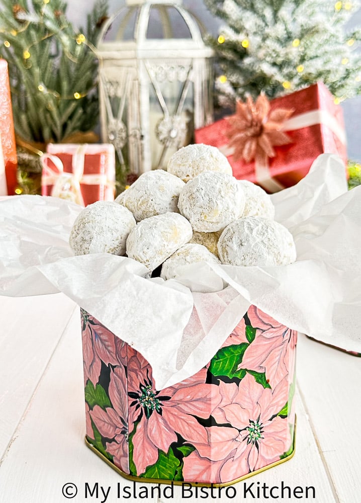 Christmas Gift Tin Filled with Mexican Wedding Cookies. Pink wrapped presents appear in the background