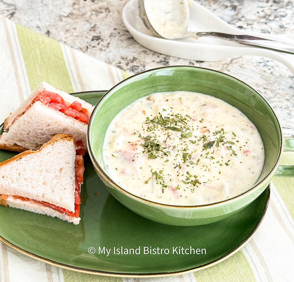 Green soup bowl filled with Ham Chowder accompanied by a tomato sandwich