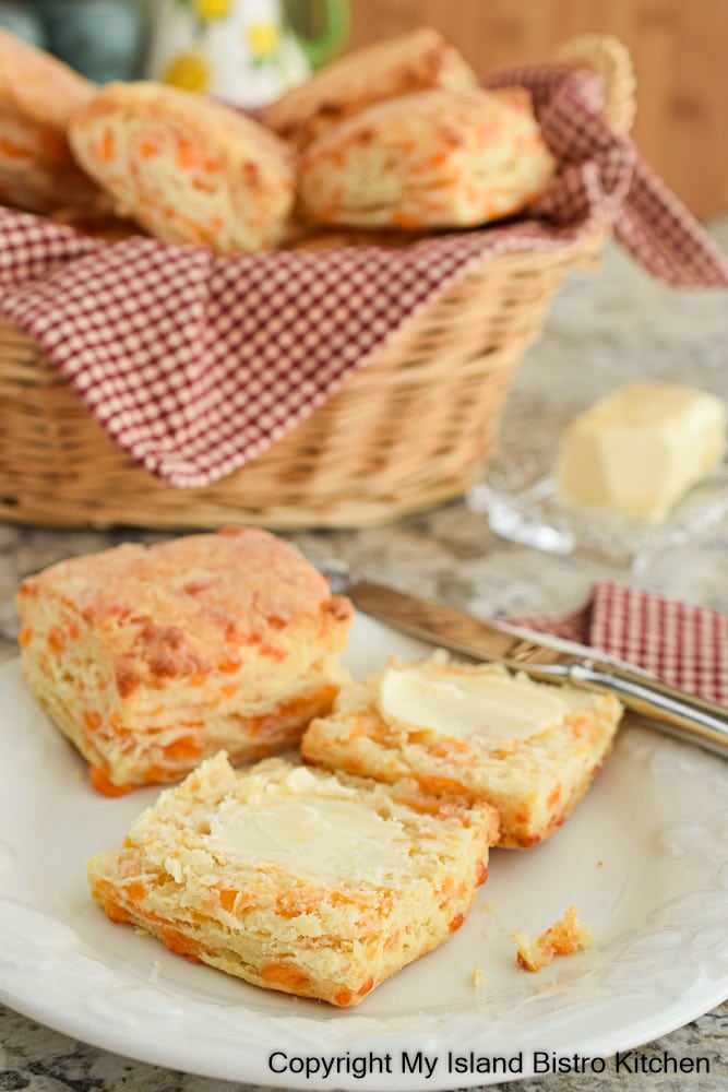 Split cheese biscuit topped with butter with basket of biscuits in background