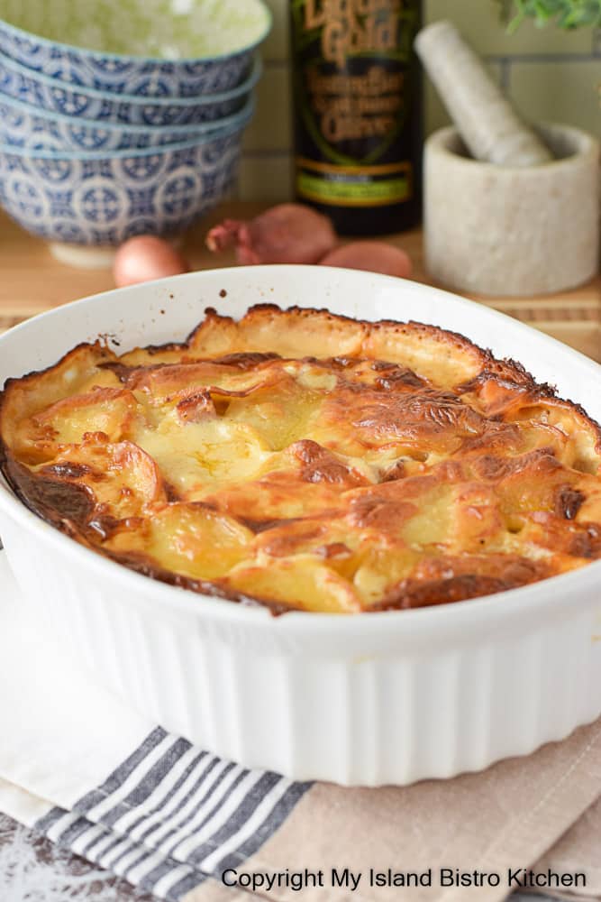 White casserole dish filled with Sliced Potatoes, Diced Ham Smothered in a Rich Cheese Sauce