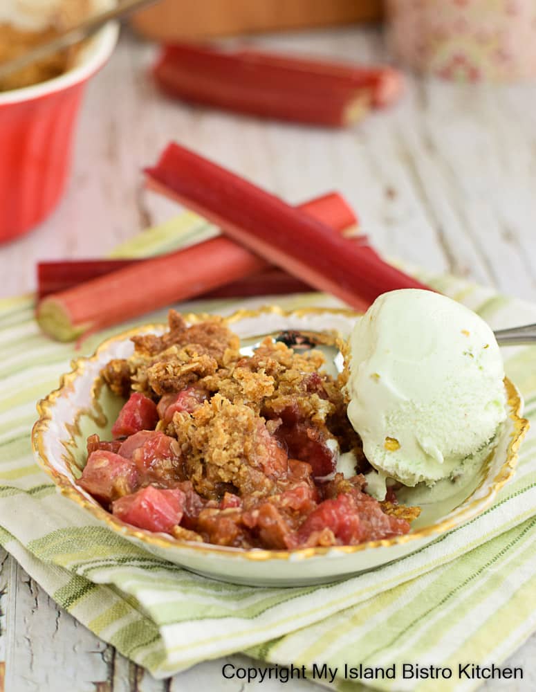 Fruit Crisp Topped with Ice Cream. Rhubarb Stalks appear in the background.