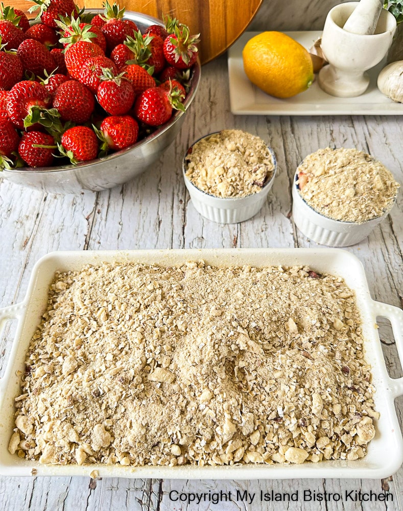 A white casserole and two ramekins filled with a fruit dessert covered in a streusel topping