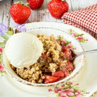 Dessert dish filled with a streusel-topped fruit crisp. A scoop of ice cream tops the crisp that is surrounded by fresh strawberries