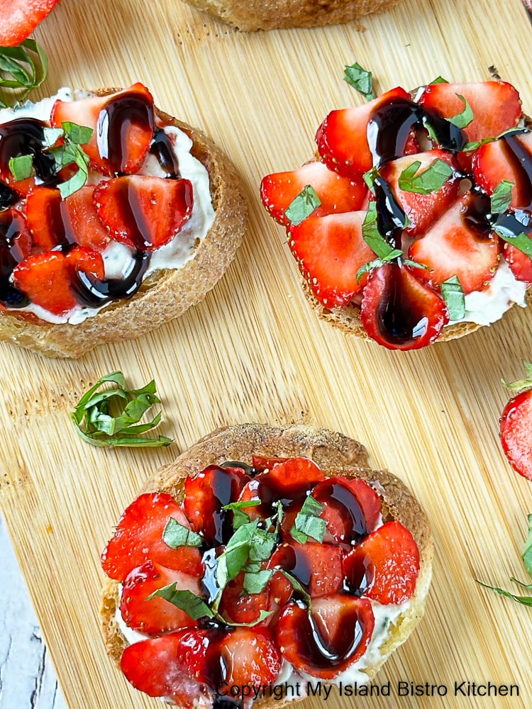 Strawberry hors d'oeuvres topped with balsamic glaze and garnished with basil chiffonade sit on wooden serving board 