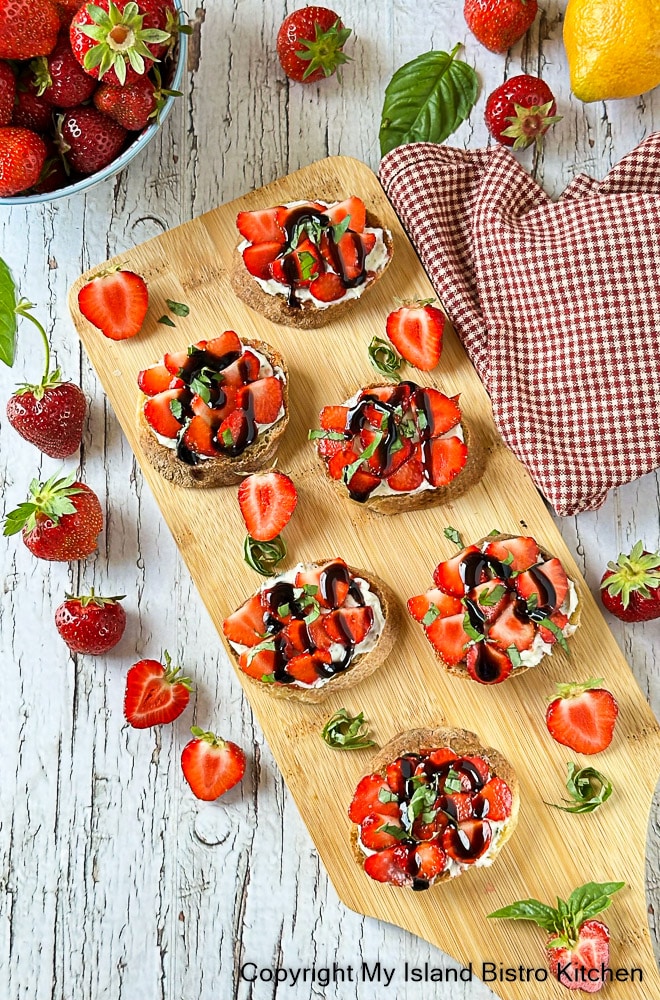 Serving board with strawberry-topped crostini surrounded by fresh strawberries