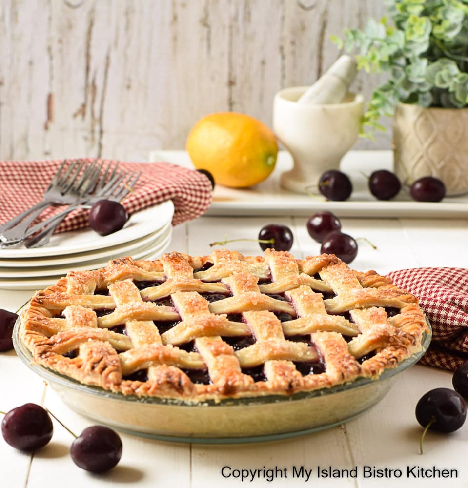 Lattice-topped Cherry Pie sits on counter with plates and napkins in background