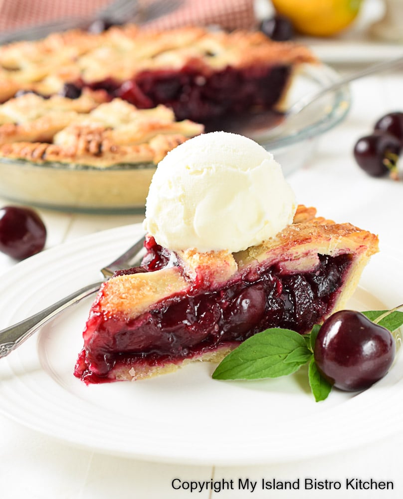 Slice of pie topped with vanilla ice cream on white plate. Pie in pie plate is in background